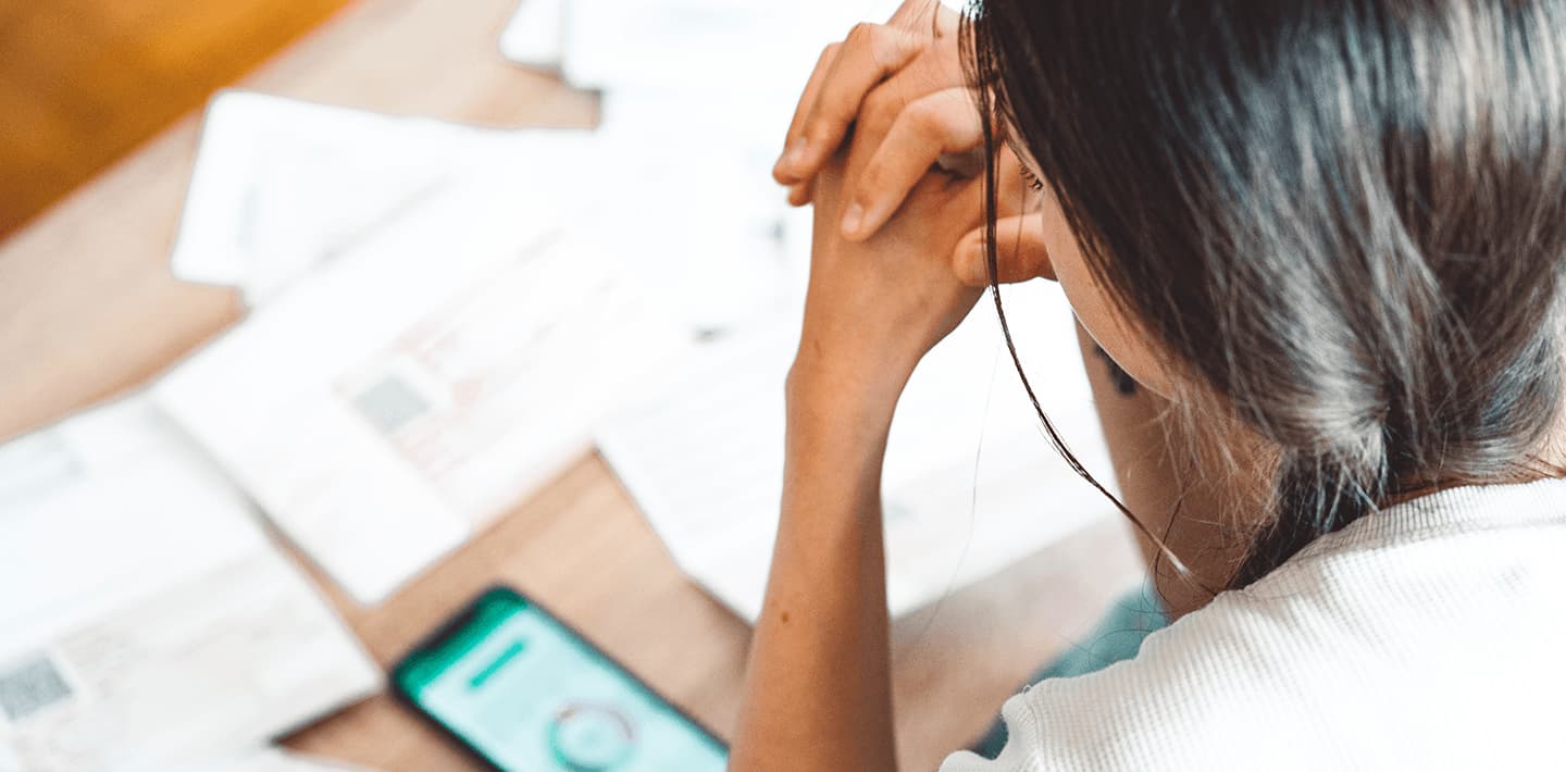 Woman looking at her phone with bills spread out in front of her