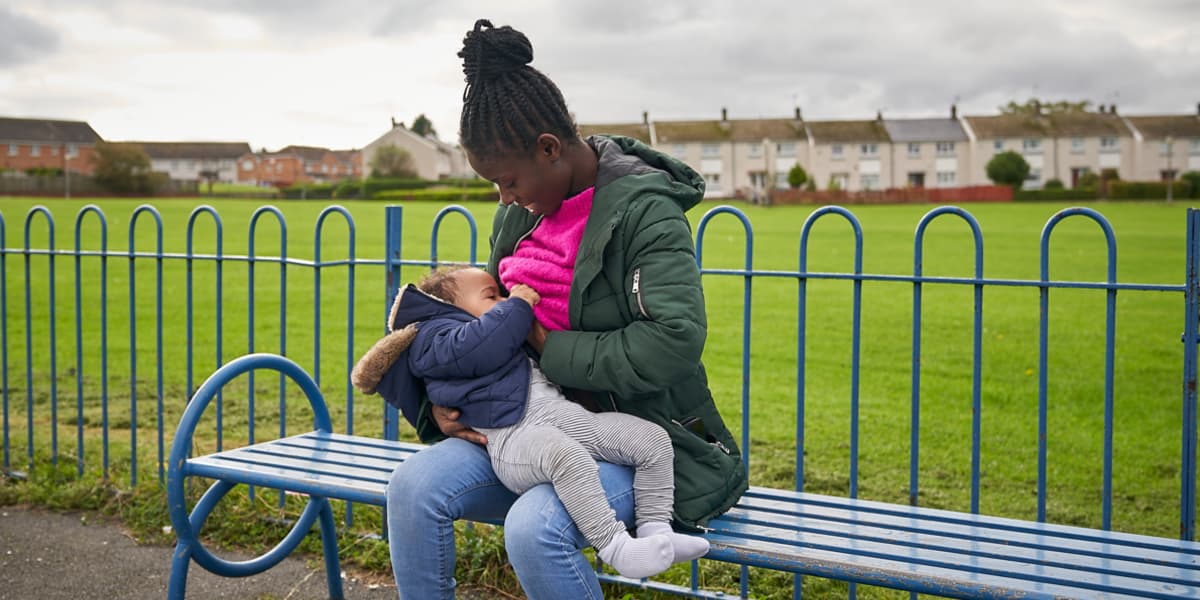 Mother breastfeeding baby outdoors, sitting on a bench