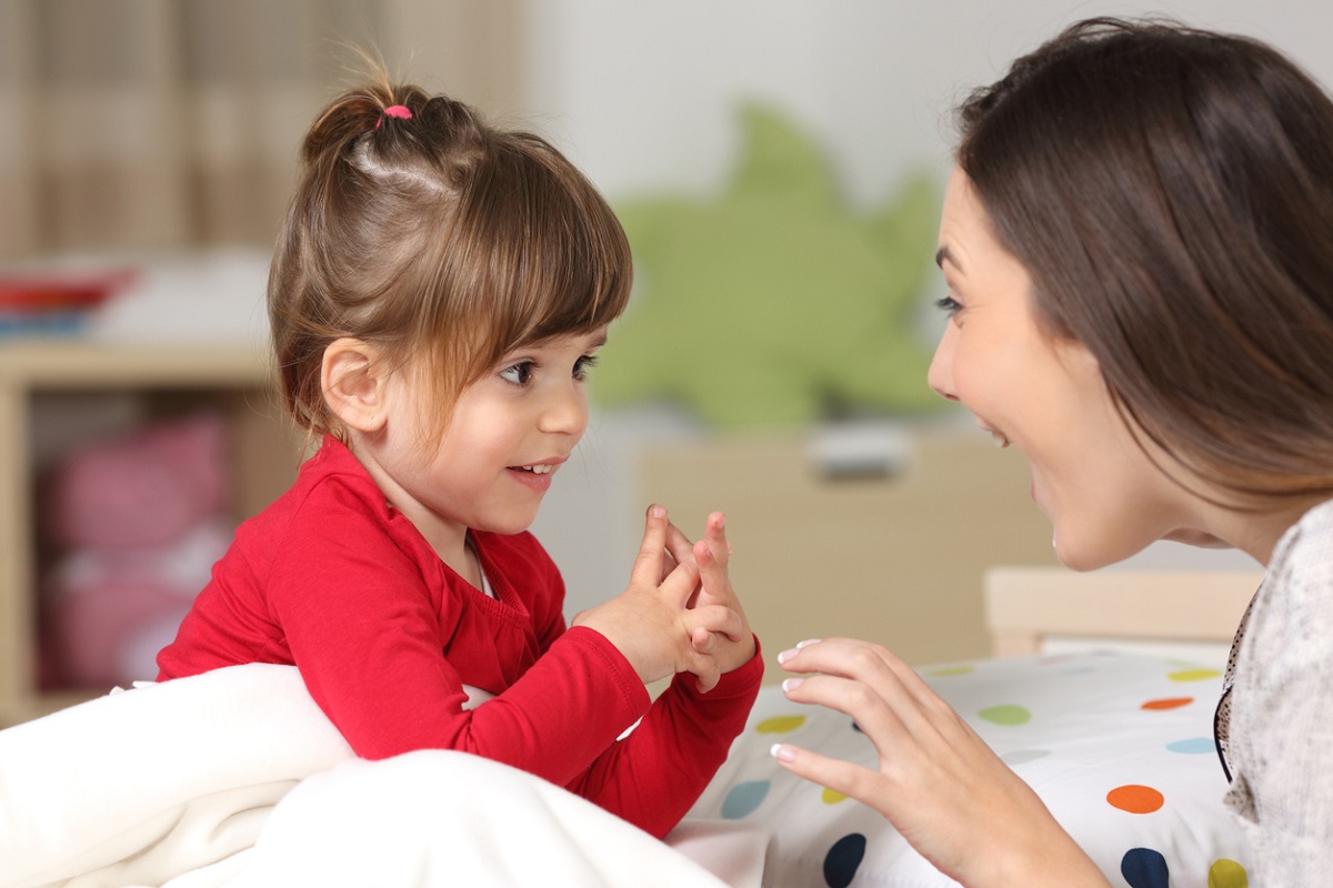 Mother talking to her toddler daughter, who's wearing a red cardigan