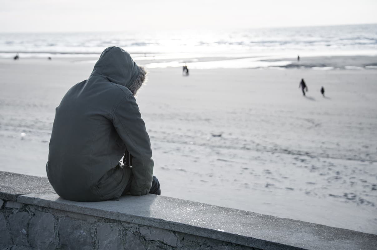 Sad teenager with their back to the camera, looking out over a beach