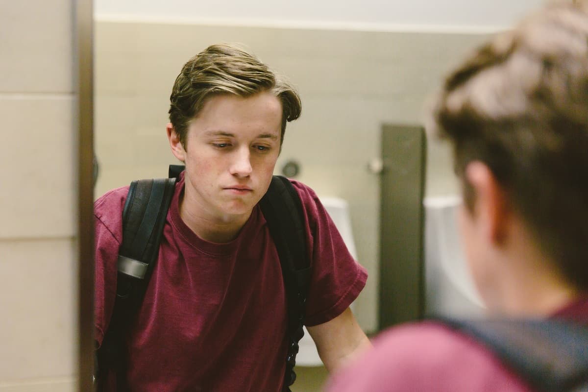 Teen boy looking in the mirror, looking down