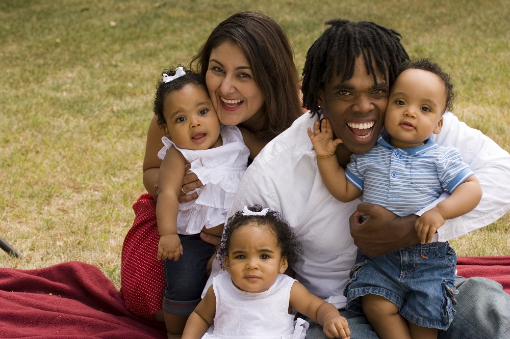Triplet toddlers on a picnic rug with their parents