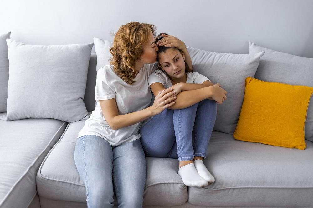 Mum hugging sad teen daughter on the sofa