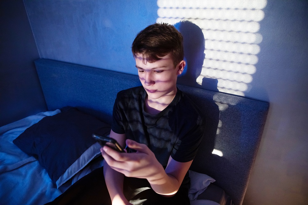 Teenage boy in his bedroom, staring at his phone, looking lonely