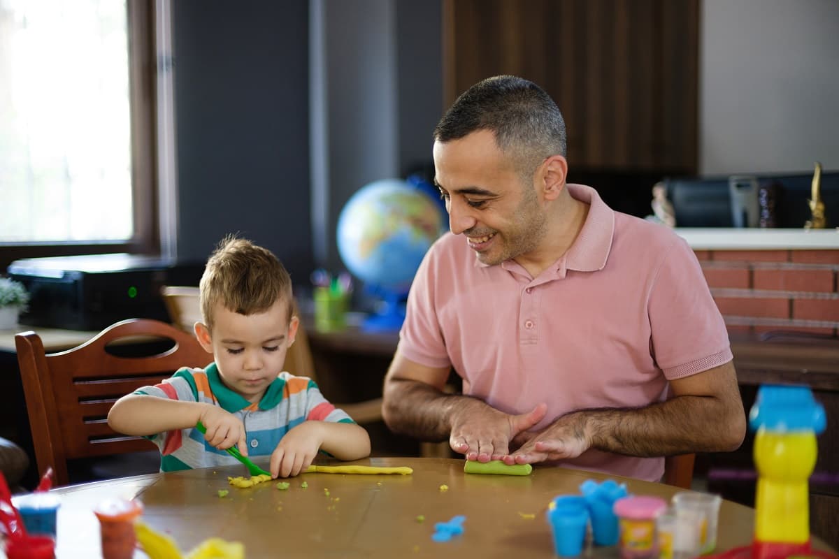 Dad and toddler boy playing with playdough at a table