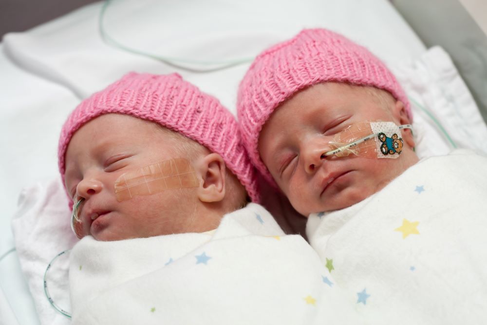 Premature twin babies in a neonatal unit, wearing knitted pink hats