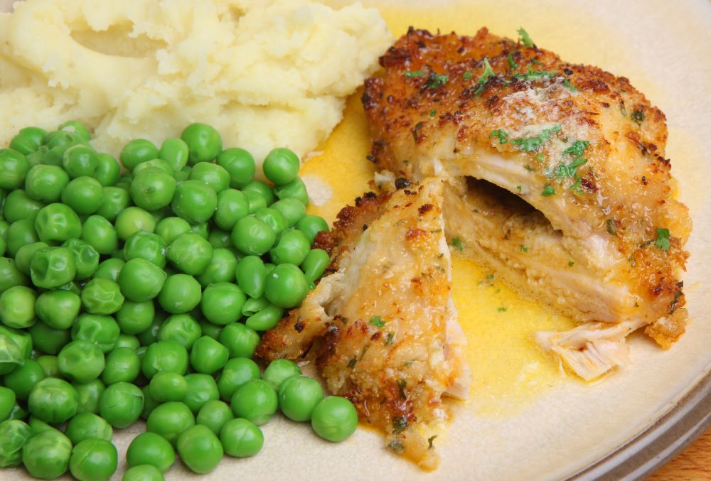 Chicken kiev with mashed potato and peas.