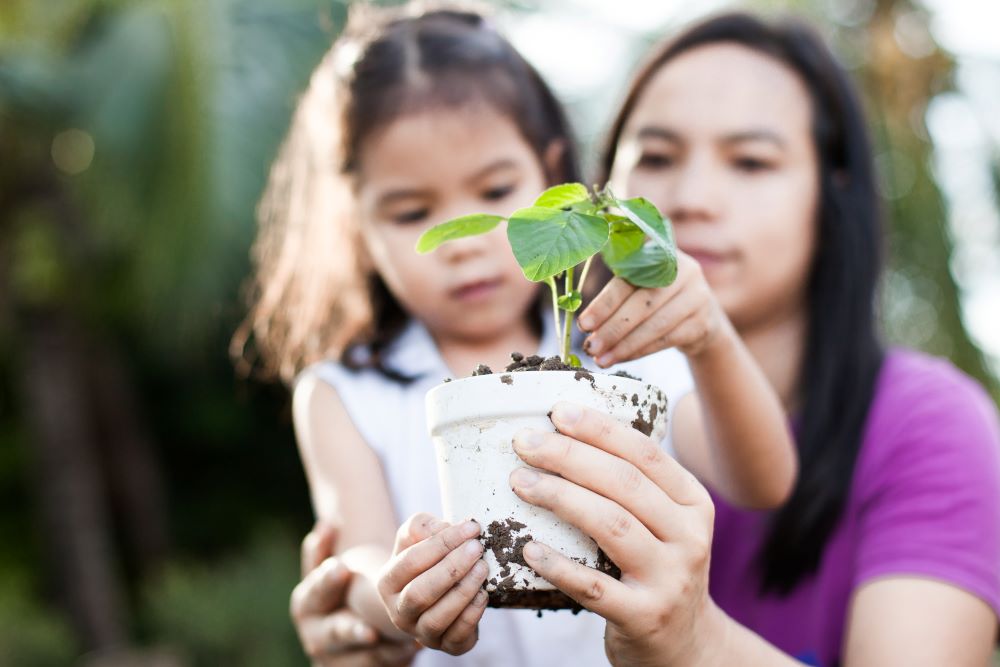 Mum and daughter outside, holding up a plant in a pot.