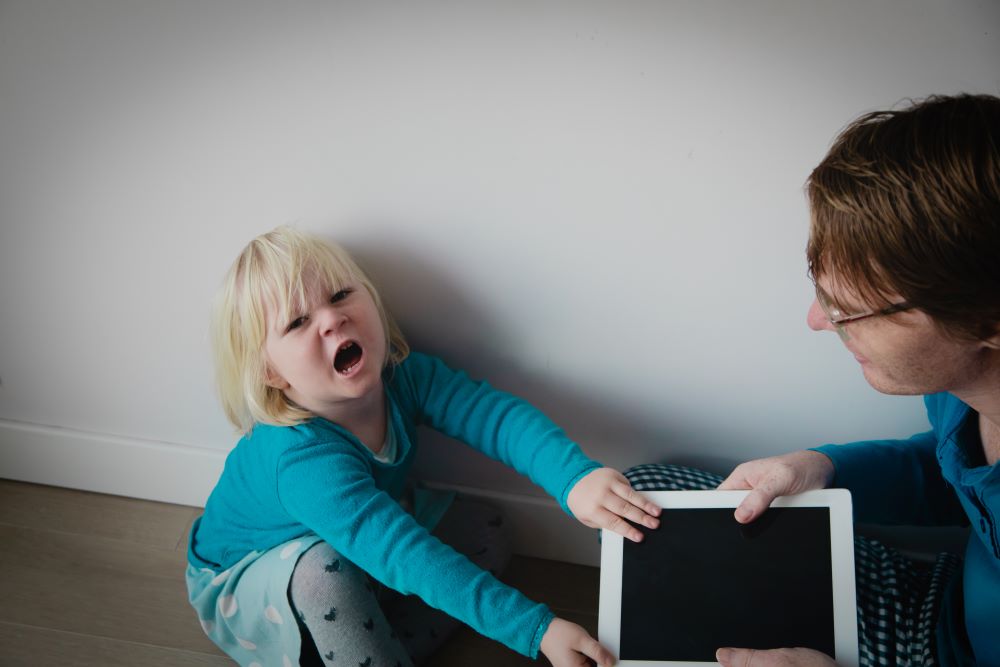 A mother trying to take a tablet away from a screaming child.