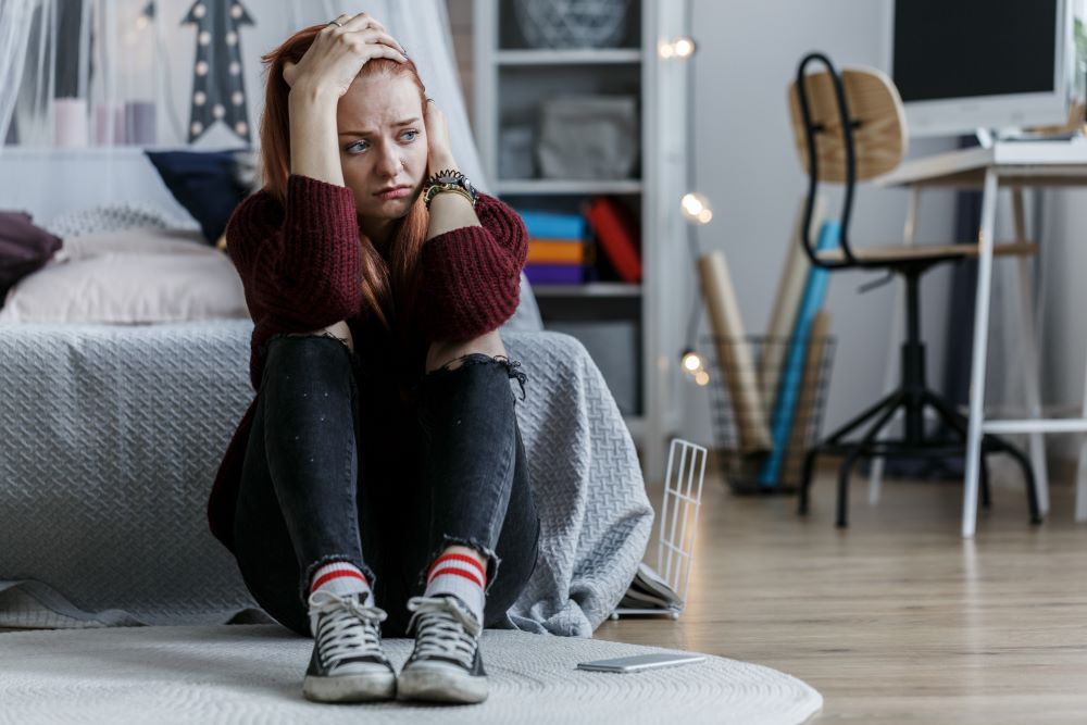 Anxious teenage girl sitting on the floor in her bedroom.