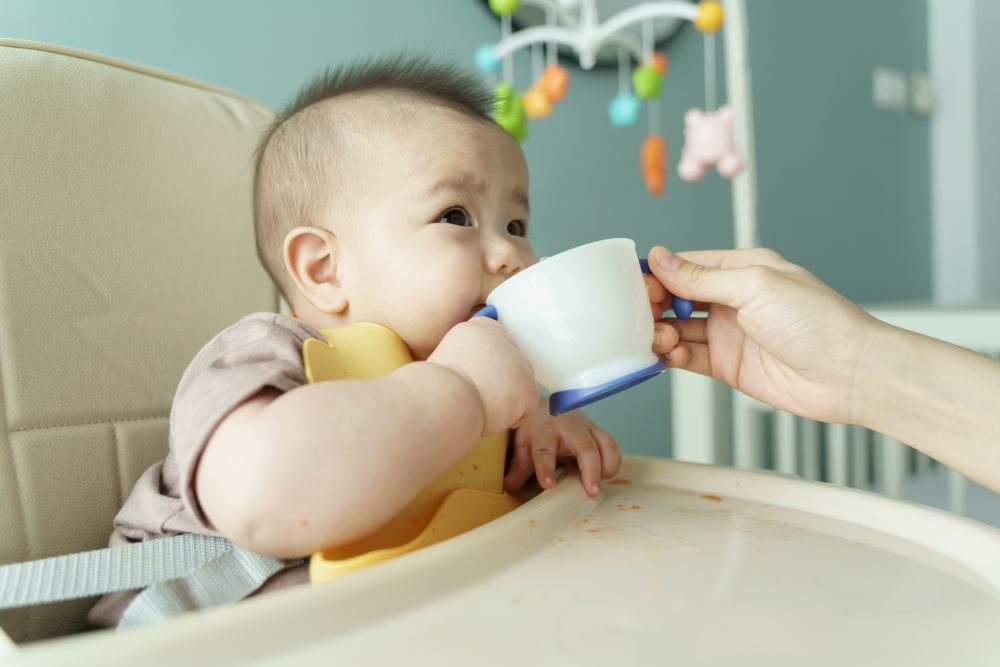 Baby sitting in a highchair drinking from a cup