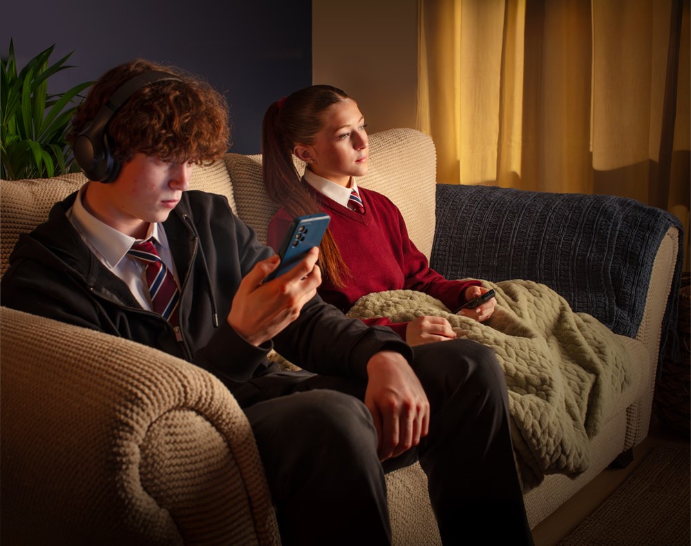 Boy and girl sitting on a sofa, the boy looking at his phone.