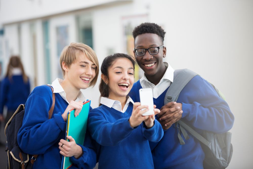 Teenage boy and girls wearing school uniform, smiling while taking a selfie.