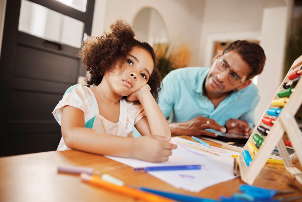 Young girl staring into the distance while her dad helps her with her homework.