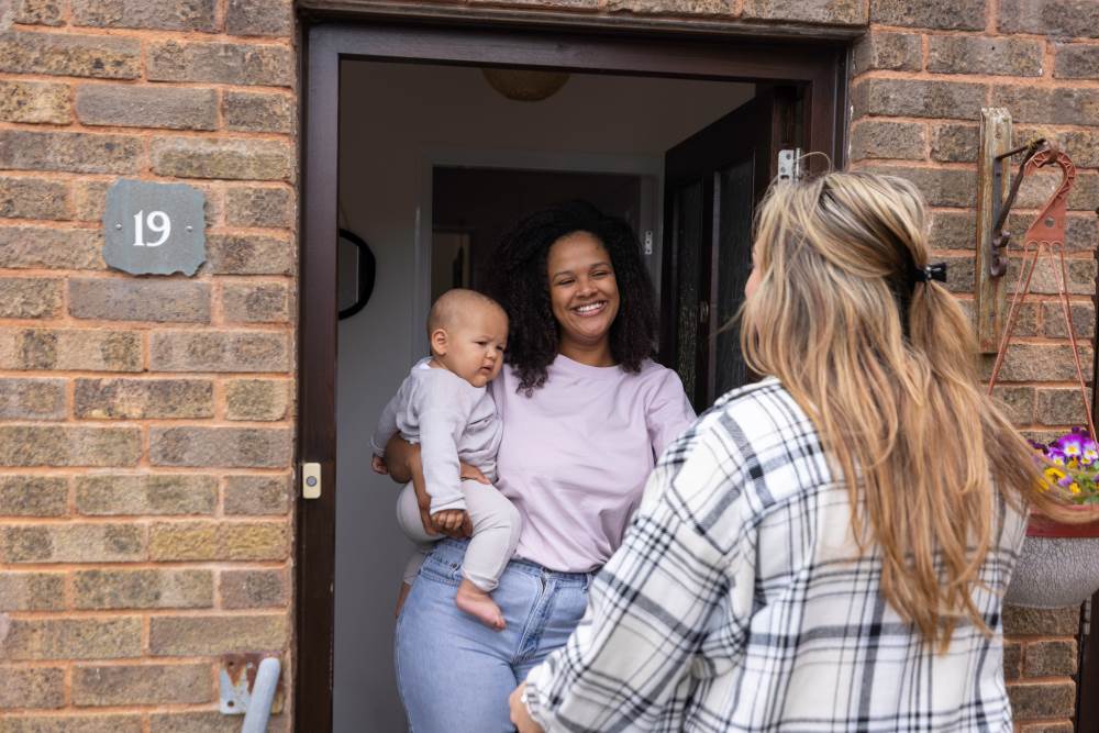 Mum and baby greeting their health visitor at the door.