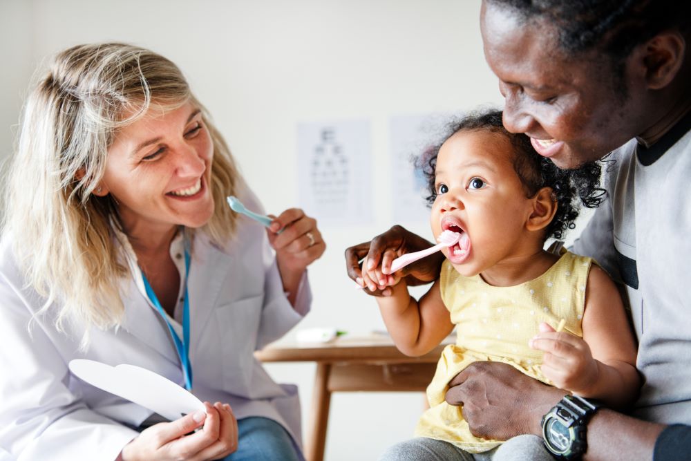 Health visitor talking to mother and toddler, showing the toddler how to brush her teeth.
