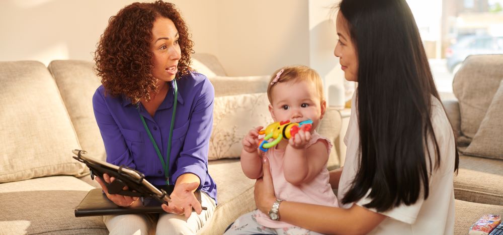 Health visitor showing a mother and baby information on a tablet.
