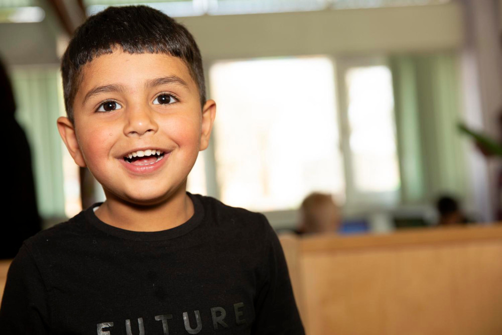 Image of a child looking above the camera with a big smile on their face.