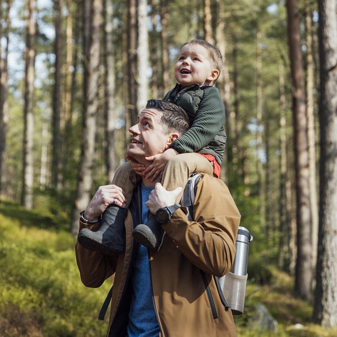 Happy toddler sitting on dad's shoulders, outdoors in a wood