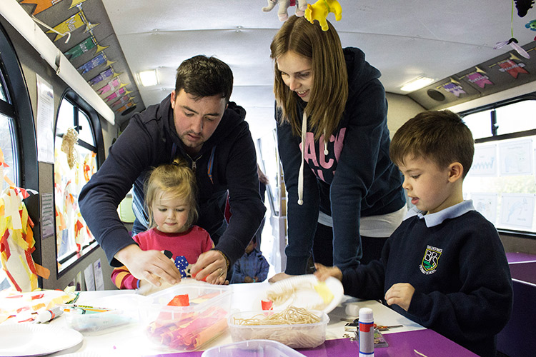 Image of a mum, a dad and their two children on a bus doing crafts.