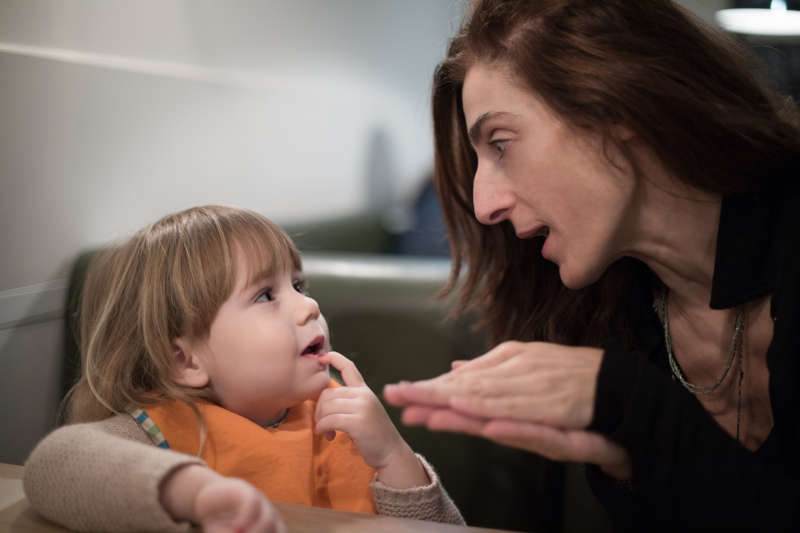 Image of a mum hiding something in her hands and her toddler looking at her trying to guess what it is.