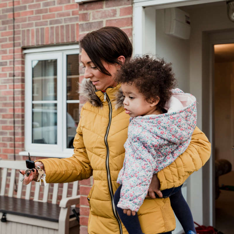 Image of a mum carrying her toddler out of the front door of their house.