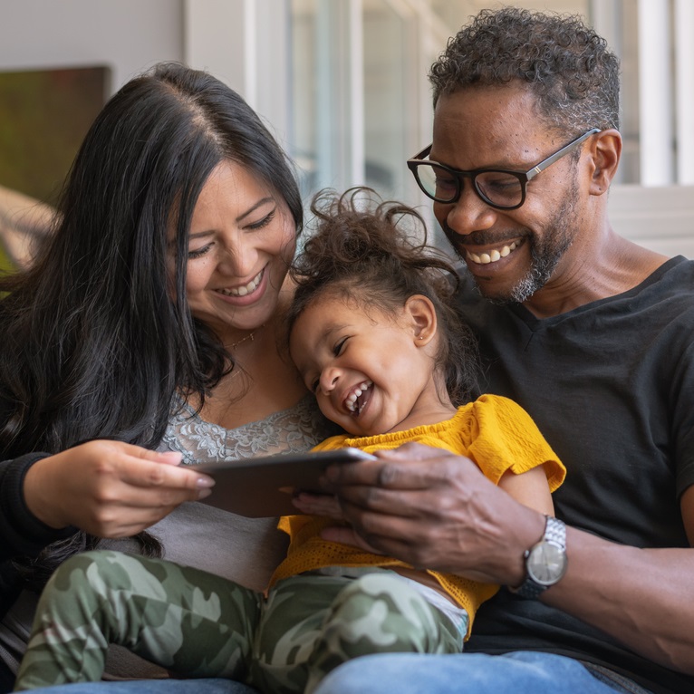 Mother and father with toddler laughing together while looking at a phone