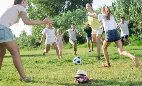 Teens and older children playing football in the park on a sunny day