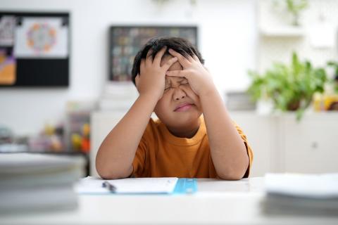 Young boy covering his face because he's stuck on his homework