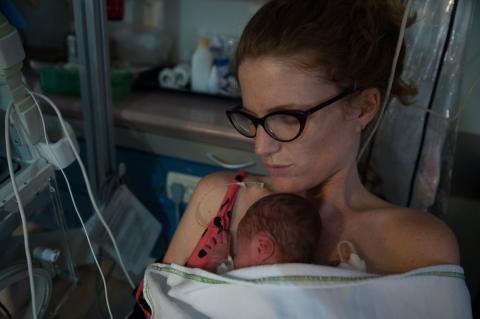 Mum holding premature baby next to her skin in a neonatal unit.