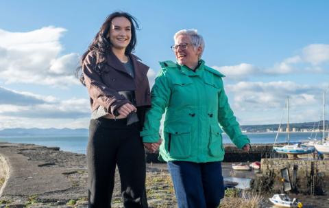 Daughter and mother on a beach, smiling at each other.
