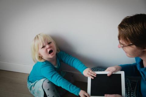 A mother trying to take a tablet away from a screaming child.