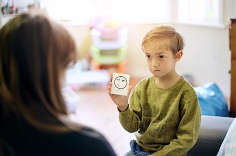 Small boy holding up a card with a puzzled-looking face on it.
