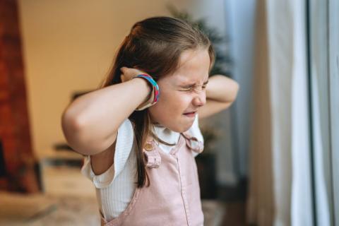 Young girl with her hands over her ears and her eyes squeezed tight shut.