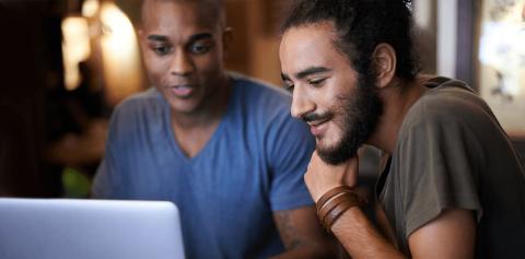 Two men looking at a laptop together, with papers around them