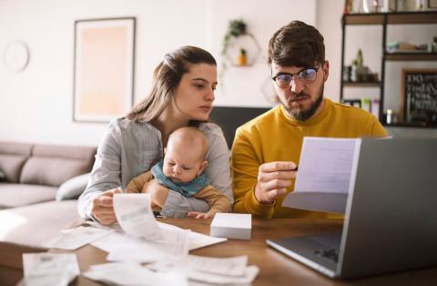 Mum and dad with baby looking at forms, with laptop open in front of them