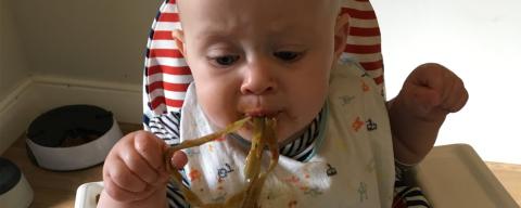 baby in highchair eating pasta noodles