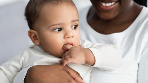 Mum holding baby, baby is sucking their fingers