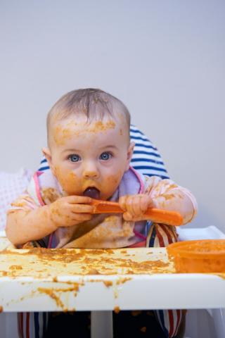 baby in a high chair eating carrots messily