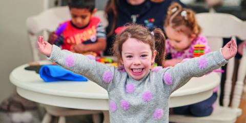 Image of a child in a playroom with a big smile on their face and their arms outstretched wide.