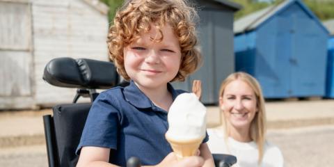 Child in wheelchair at the beach, holding an ice cream