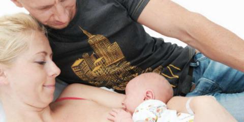 Photo of a couple looking at their newborn while the mother breastfeeds her baby 