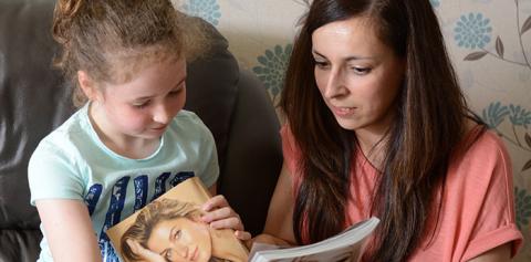 Image of a mum and child sitting together on a sofa and reading a magazine.