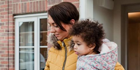 Image of a mum carrying her toddler out of the front door of their house.