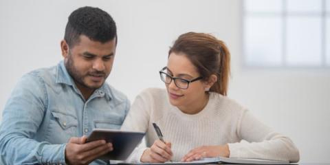 Image of two parents sitting at a table looking at a tablet and writing.