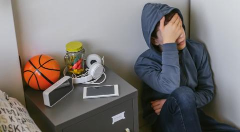 Teen boy sitting on the floor in his bedroom with his hand over his face