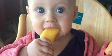 Baby sitting in a high chair eating a banana